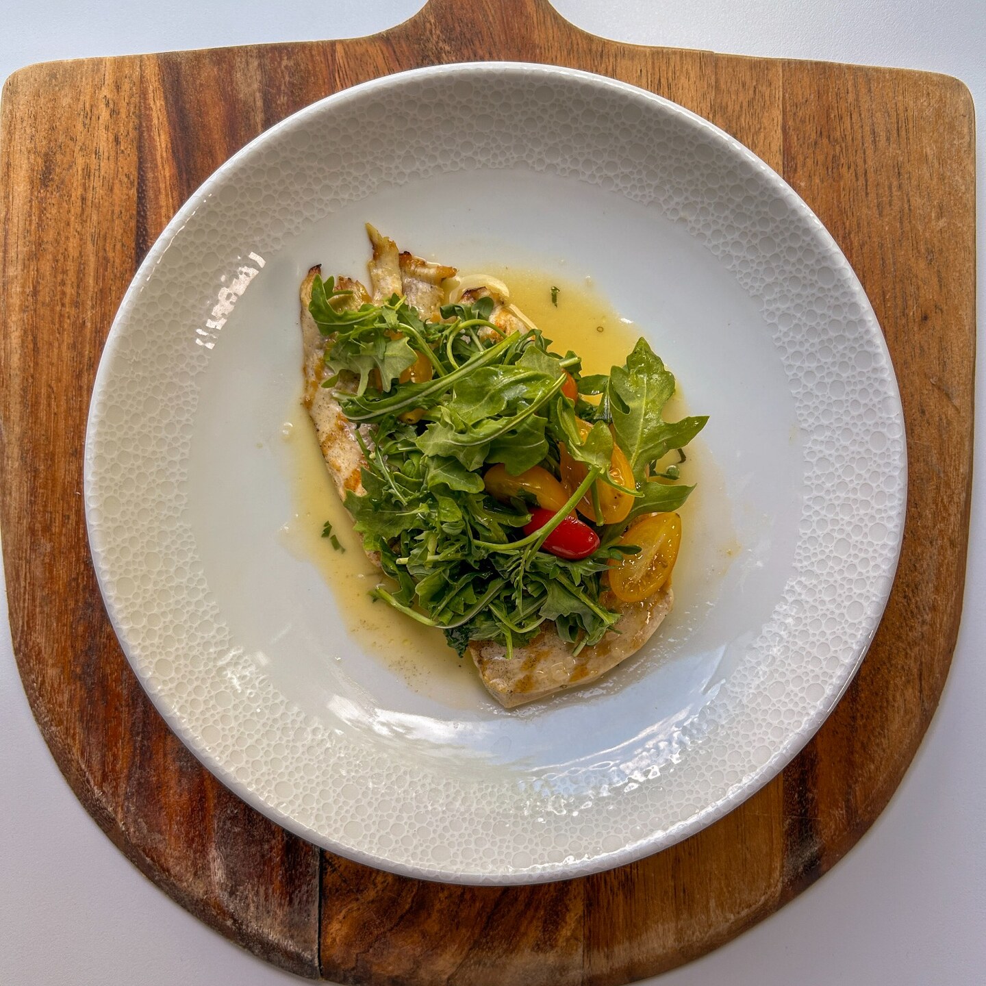Overhead view of grilled chicken topped with arugula and tomatoes on a wooden serving board