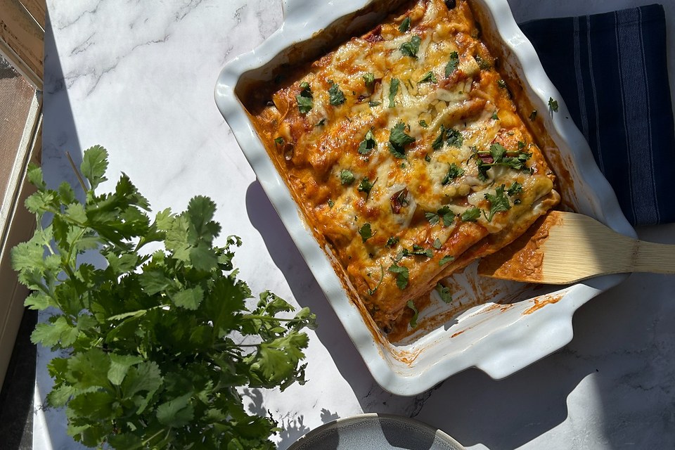 Sunlit baked lasagna served from a ceramic dish beside fresh cilantro