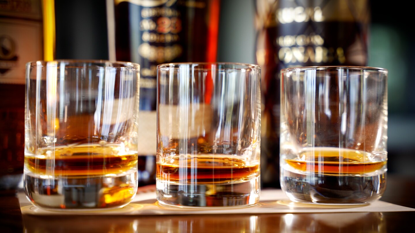 Three glasses of amber rum lit against a softly blurred bar